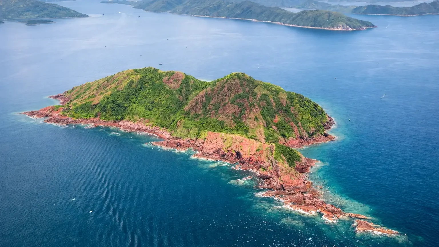 Aerial view of Port Island (Chek Chau) in northeast Hong Kong showing red sedimentary rock cliffs surrounded by clear blue sea in the Hong Kong UNESCO Global Geopark