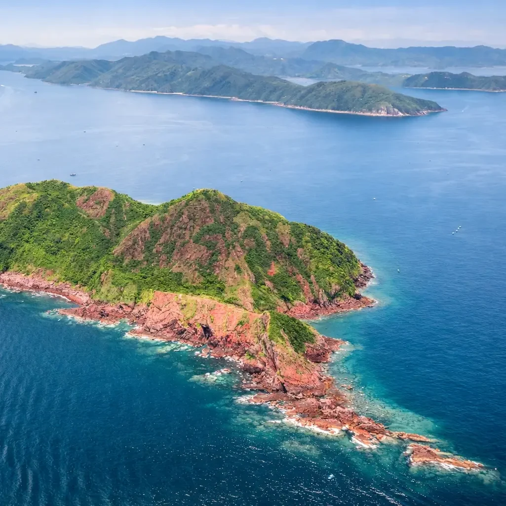 Aerial view of Port Island (Chek Chau) in northeast Hong Kong showing red sedimentary rock cliffs surrounded by clear blue sea in the Hong Kong UNESCO Global Geopark