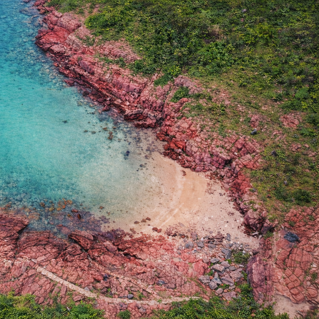 Aerial view of a small beach surrounded by red sedimentary rock cliffs on Port Island in Hong Kong UNESCO Global Geopark