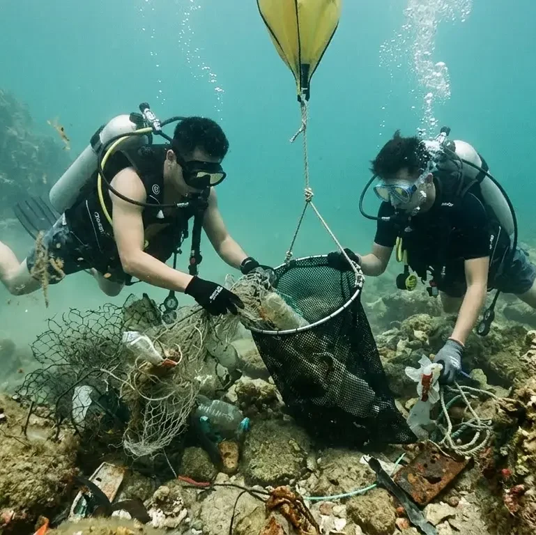 scuba divers collecting marine debris underwater in Hong Kong using mesh bag during NGO cleanup operation
